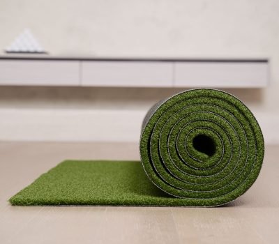 Close-up of a rolled artificial turf mat on a floor, ideal for indoor golf practice.