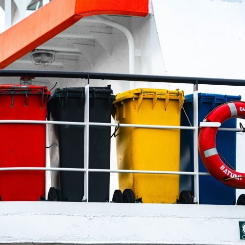Four colorful waste bins and a lifebuoy on a ship's deck, adding vibrant contrast.