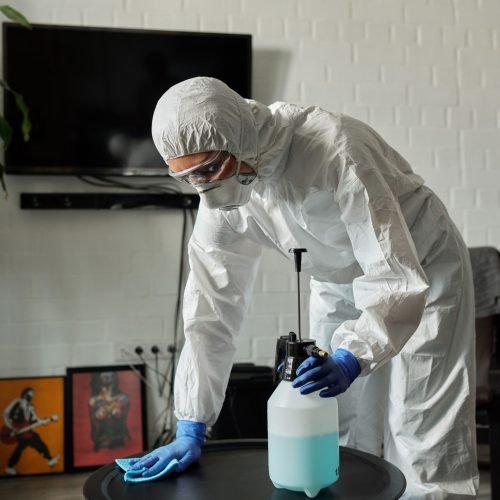 Person in protective gear cleaning a living room table with disinfectant.